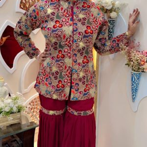 Traditional gold embroidered floral jacket paired with maroon sharara pants, styled in a boutique setup.